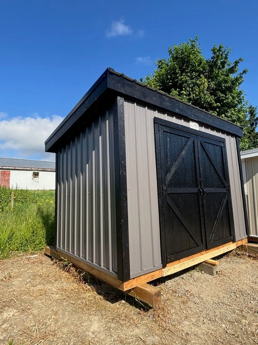 Grey metal shed with black barn doors and trim, angled view