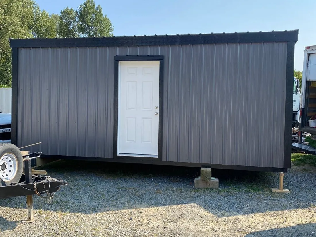 Long dark grey shed with white door on a trailer